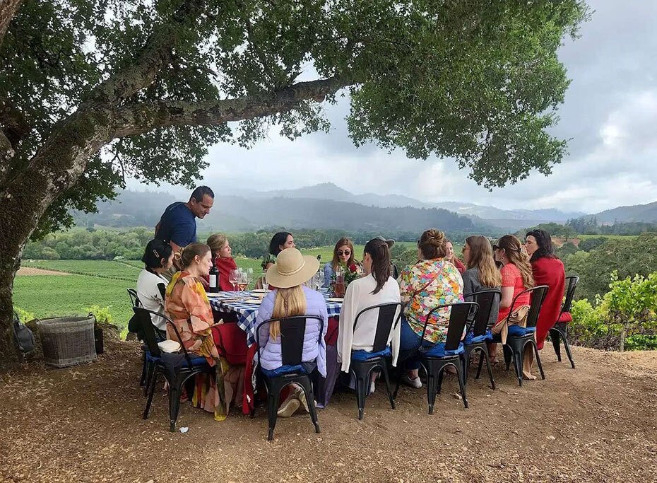 people sitting around a table on a hilltop under an oak tree