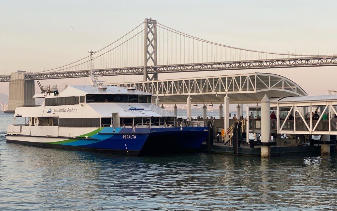 San Francisco Bay Ferry “Peralta” docked at the Ferry Building terminal with the Bay Bridge in the background at sunrise.
