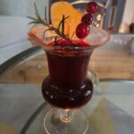 Deep red holiday mocktail served in a stemmed glass, garnished with cranberries, fresh rosemary, and a dried orange slice.