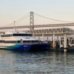 San Francisco Bay Ferry “Peralta” docked at the Ferry Building terminal with the Bay Bridge in the background at sunrise.