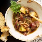 Rustic bowl of Dublin coddle with sausage, potatoes, onions, and fresh parsley garnish