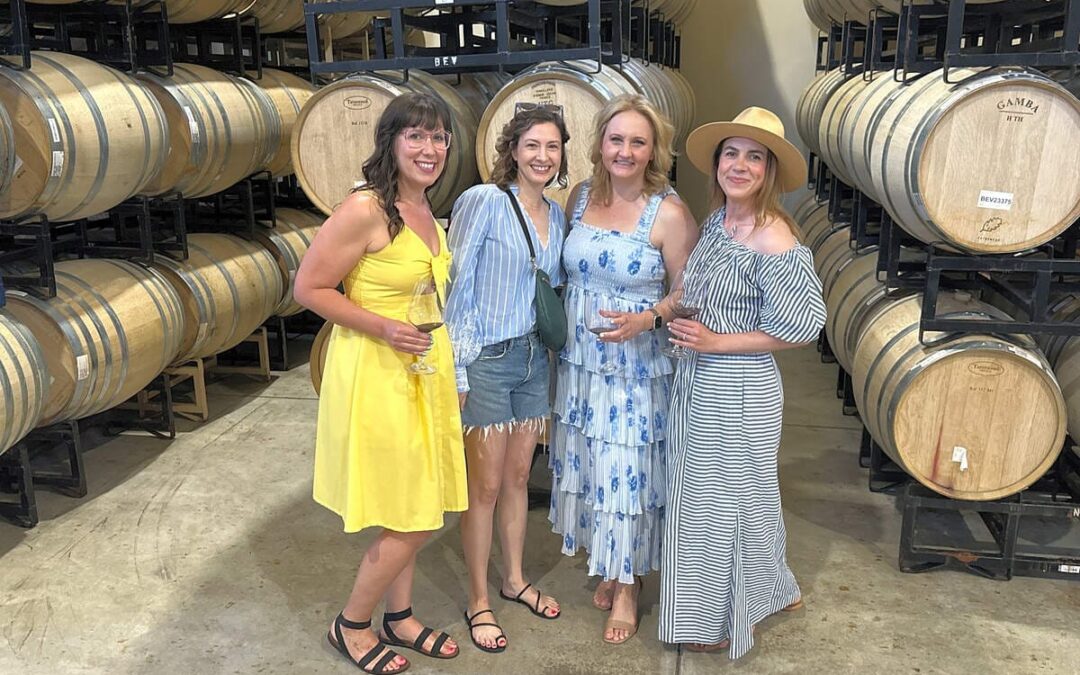 group of woman standing next to each other with wine barrels behind