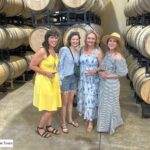 group of woman standing next to each other with wine barrels behind