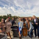 A group of coworkers enjoying a corporate wine tour in Napa Valley, standing by grape bins at a vineyard with glasses of wine and fall vineyard views in the background.
