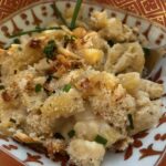 Close-up of creamy lobster mac and cheese topped with golden breadcrumbs and fresh chives, served in an ornate procelain orange-and-gold bowl