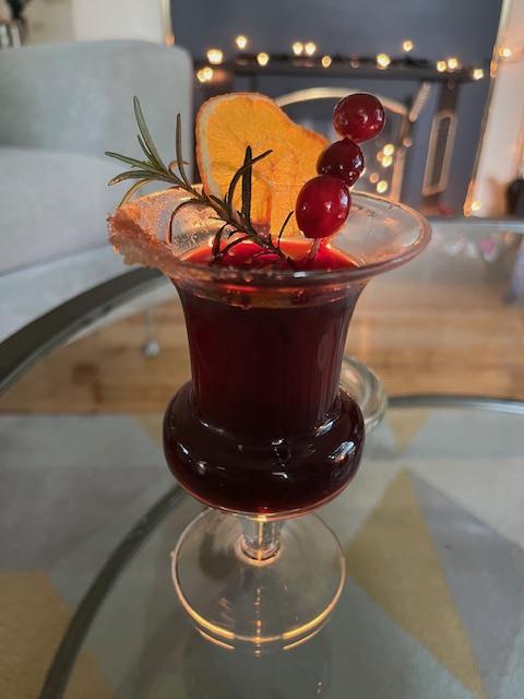 Deep red holiday mocktail served in a stemmed glass, garnished with cranberries, fresh rosemary, and a dried orange slice.