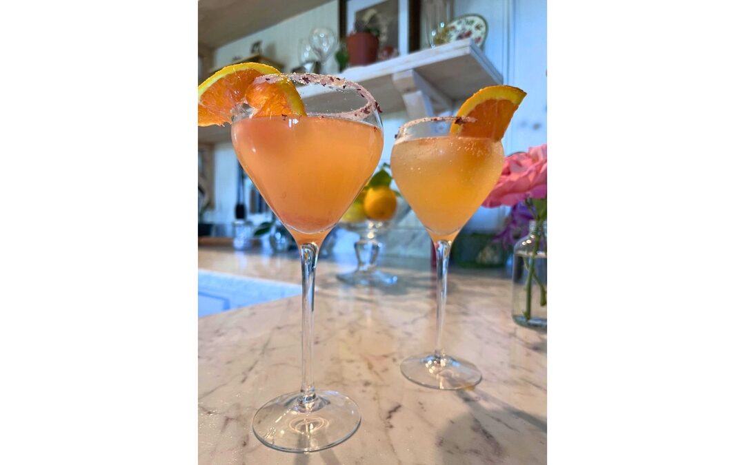 Pink grapefruit and rose Paloma cocktails in stemmed glasses with citrus garnish and rose salt rims on a marble countertop