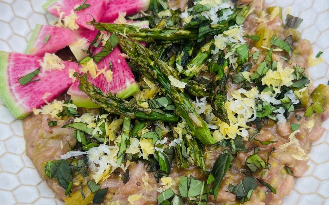 Spring risotto with asparagus and peas, topped with roasted asparagus tips, watermelon radish slices, fresh herbs, lemon zest, and grated pecorino cheese