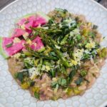 Spring risotto with asparagus and peas, topped with roasted asparagus tips, watermelon radish slices, fresh herbs, lemon zest, and grated pecorino cheese