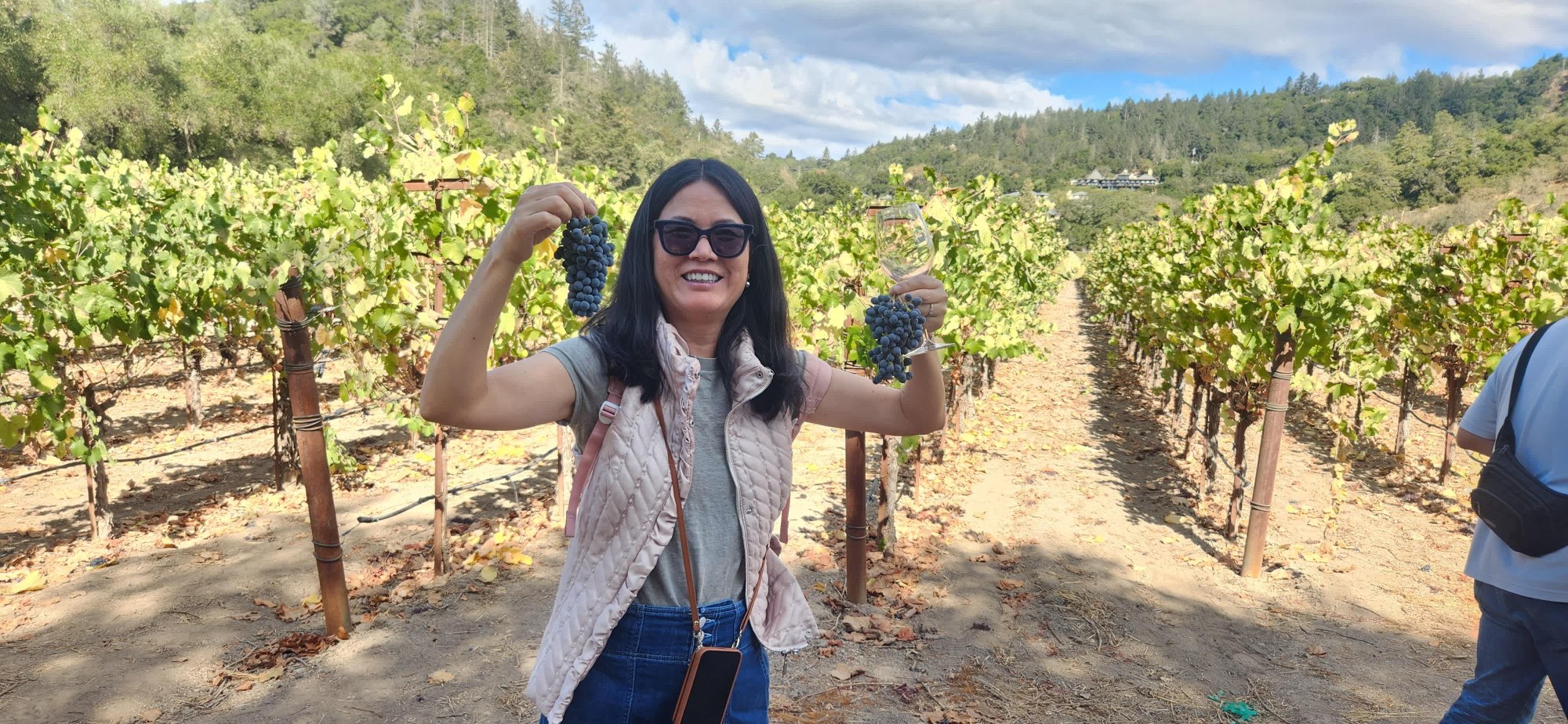 Platypus Wine Tours guest smiling and posing playfully between rows of grapevines on a sunny vineyard tour.