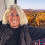 Linda, a Platypus Wine Tours guide, smiling inside the tour shuttle with autumn vineyards and Napa Valley hills visible through the window behind her.